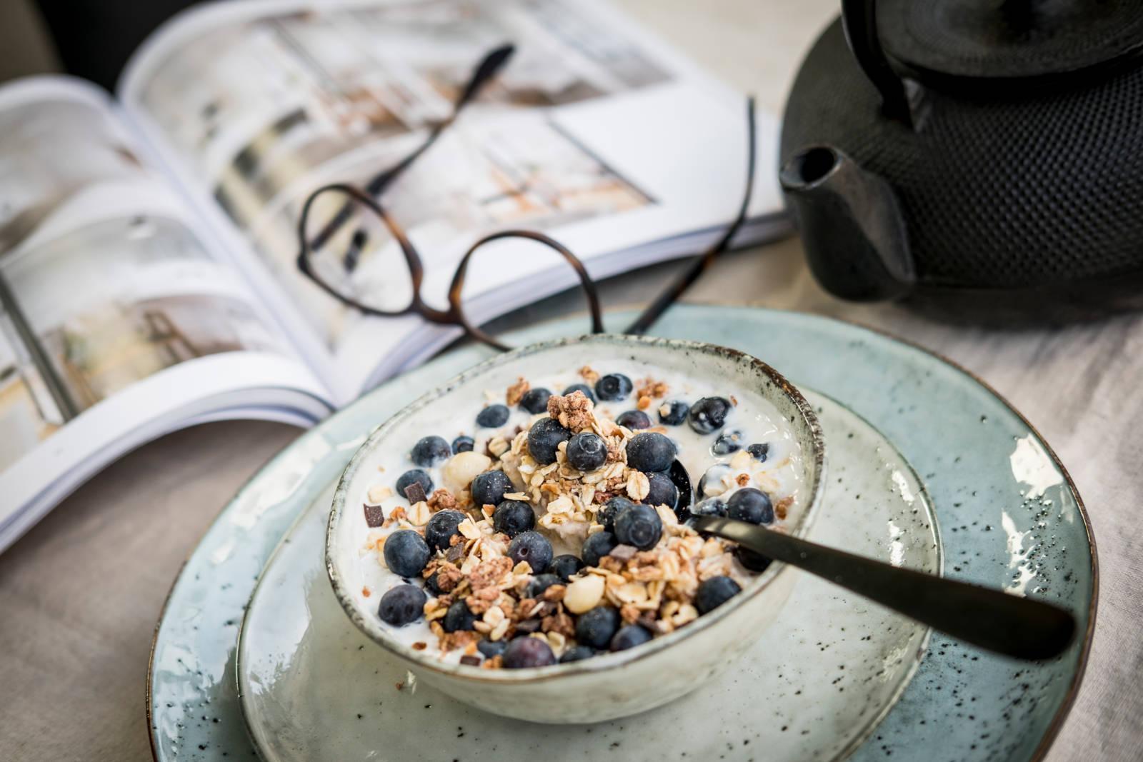 Bord med müsliskål, glasögon och en tidning.