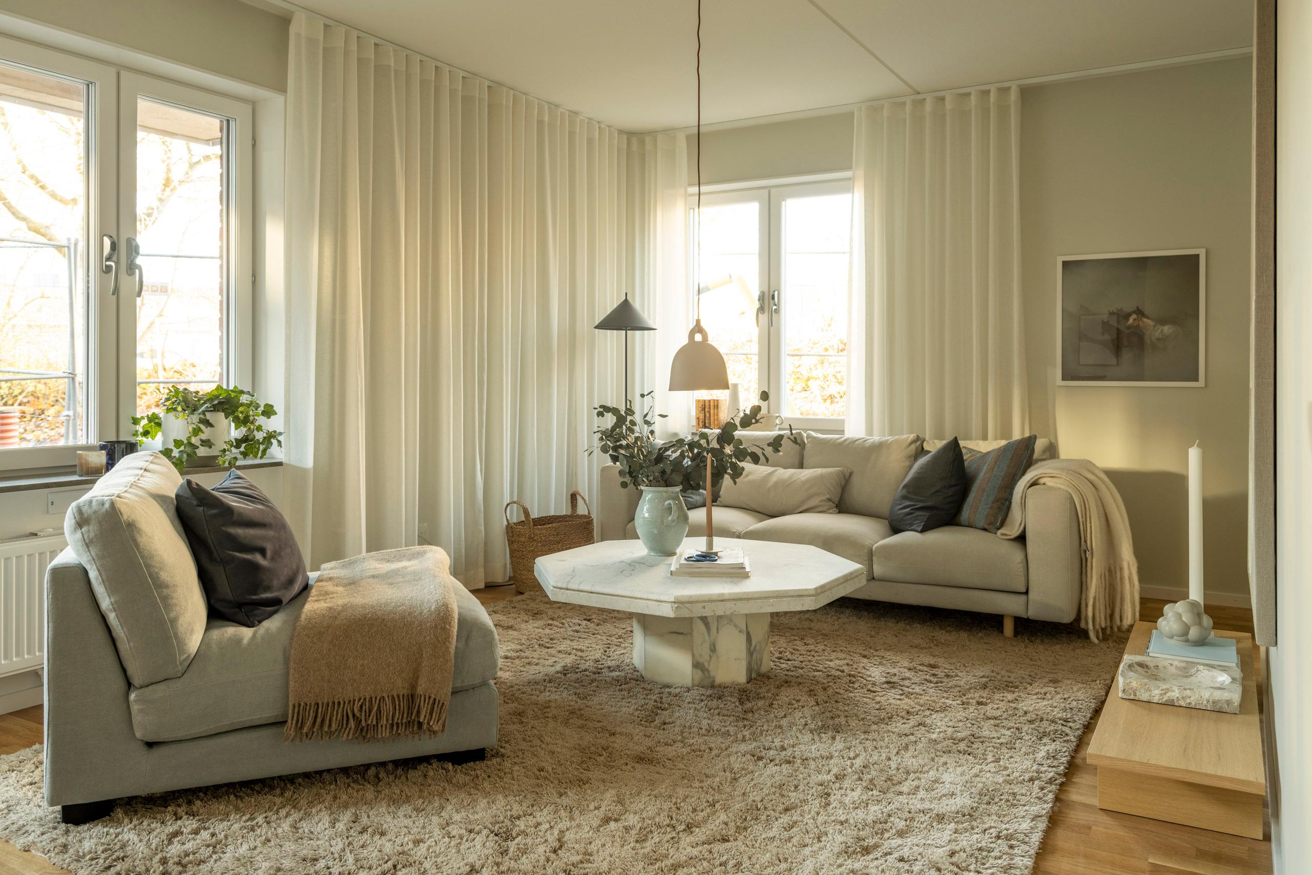 Rymligt vardagsrum i vår visningslägenhet med en stor beige soffa och fåtölj samt soffbord i sten med dekorationer på.